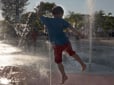 Photo of a child jumping through a jet spray of water at the Children's Fountain on the Gresham Arts Plaza