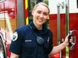 A smiling firefighter standing in front of a fire engine. 