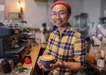 Sam Khaute, co-owner of Neo Cafe at the Rockwood Market Hall, smiles while holding a hot latte in his shop.