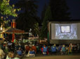 Community members sit on chairs outside on the Gresham Arts Plaza watching a featured Movies in the Park film.